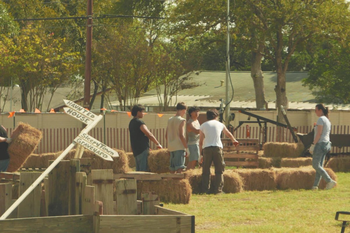 Theater’s scenic construction crew and Theatre Director Rachel Gilmour stacking a hay bale display. Actively communicating the field design desired by the Patch Staff who, shortly after, provided the volunteers with beverages. Other supplies like wooden baskets, direction signs and plank boards waiting in the field to be moved where needed.
